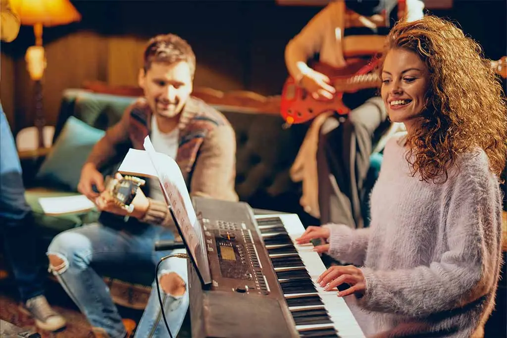 Couple playing music together. Lady plays the piano and he plays the guitar