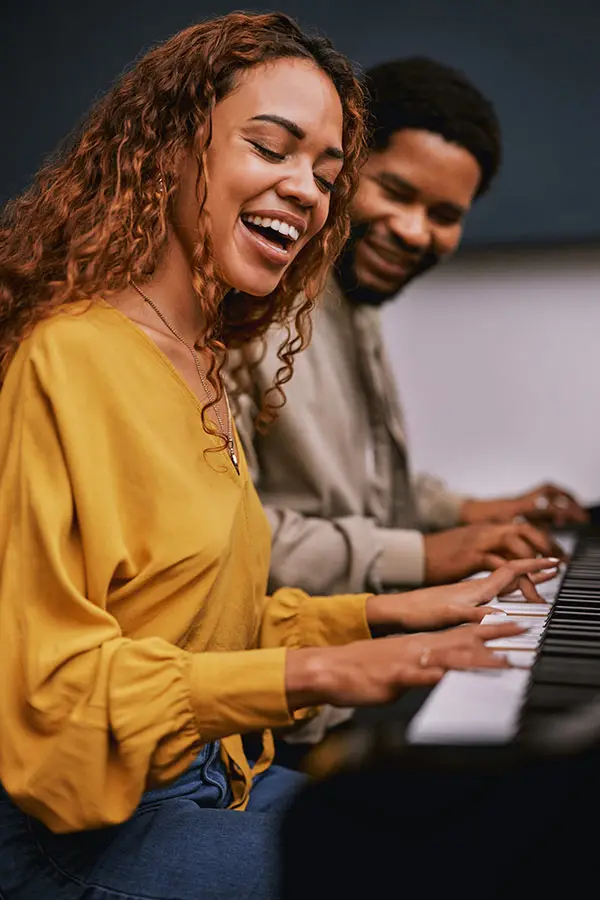 Two adults smiling while playing piano together