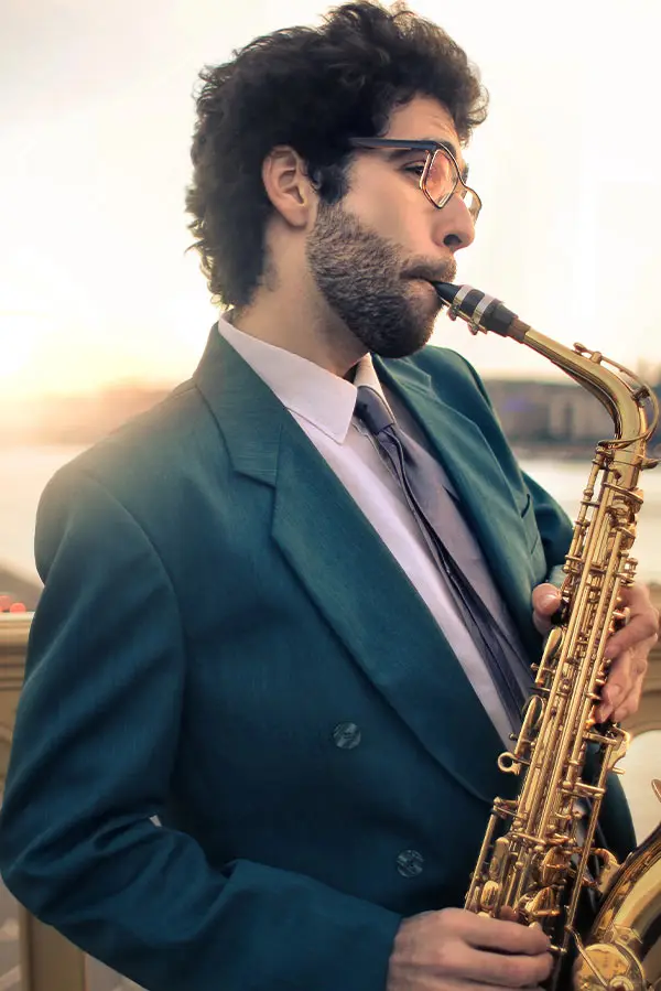 Bearded man in a teal suit playing alto saxophone at sunset