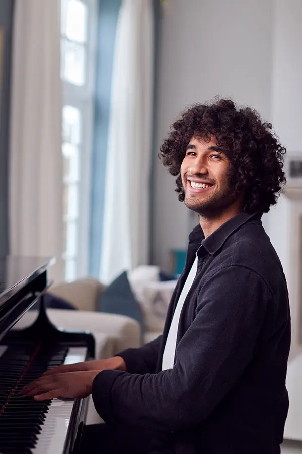 Smiling curly-haired man playing piano indoors