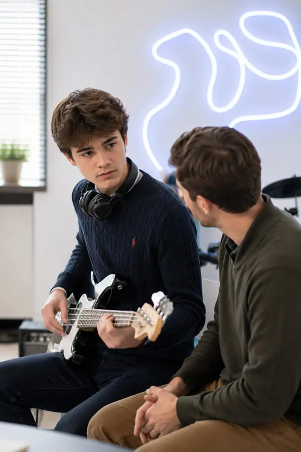 Student holding an electric bass guitar beside a teacher