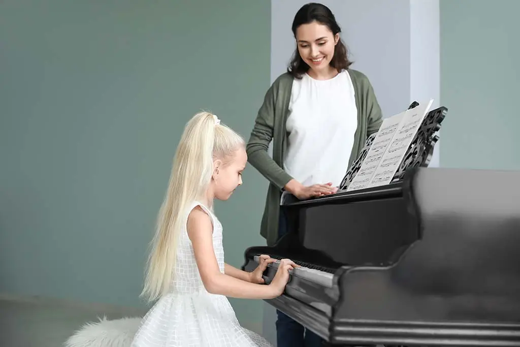Young girl playing grand piano with a teacher beside her
