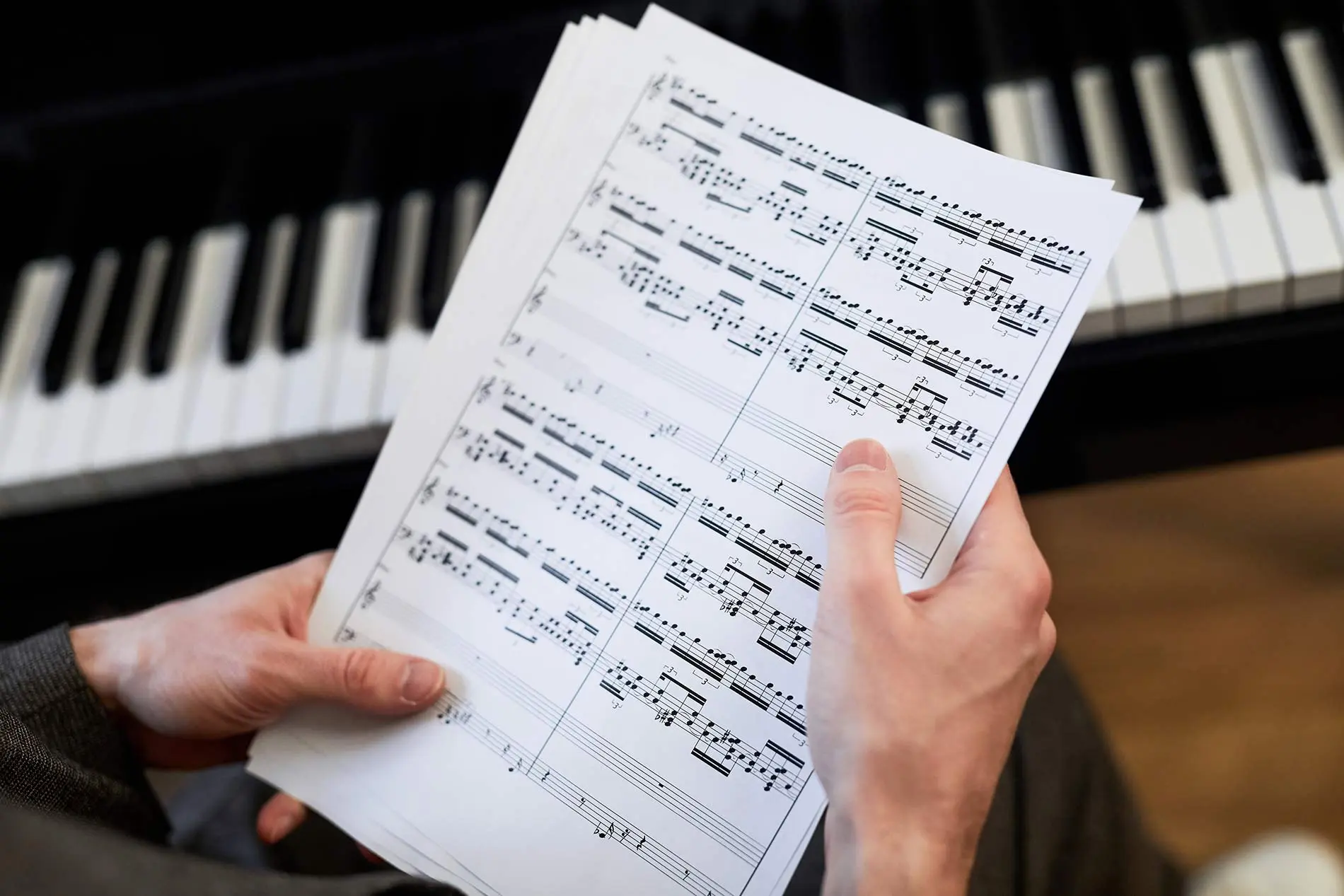 Hands holding sheet music with piano on the background