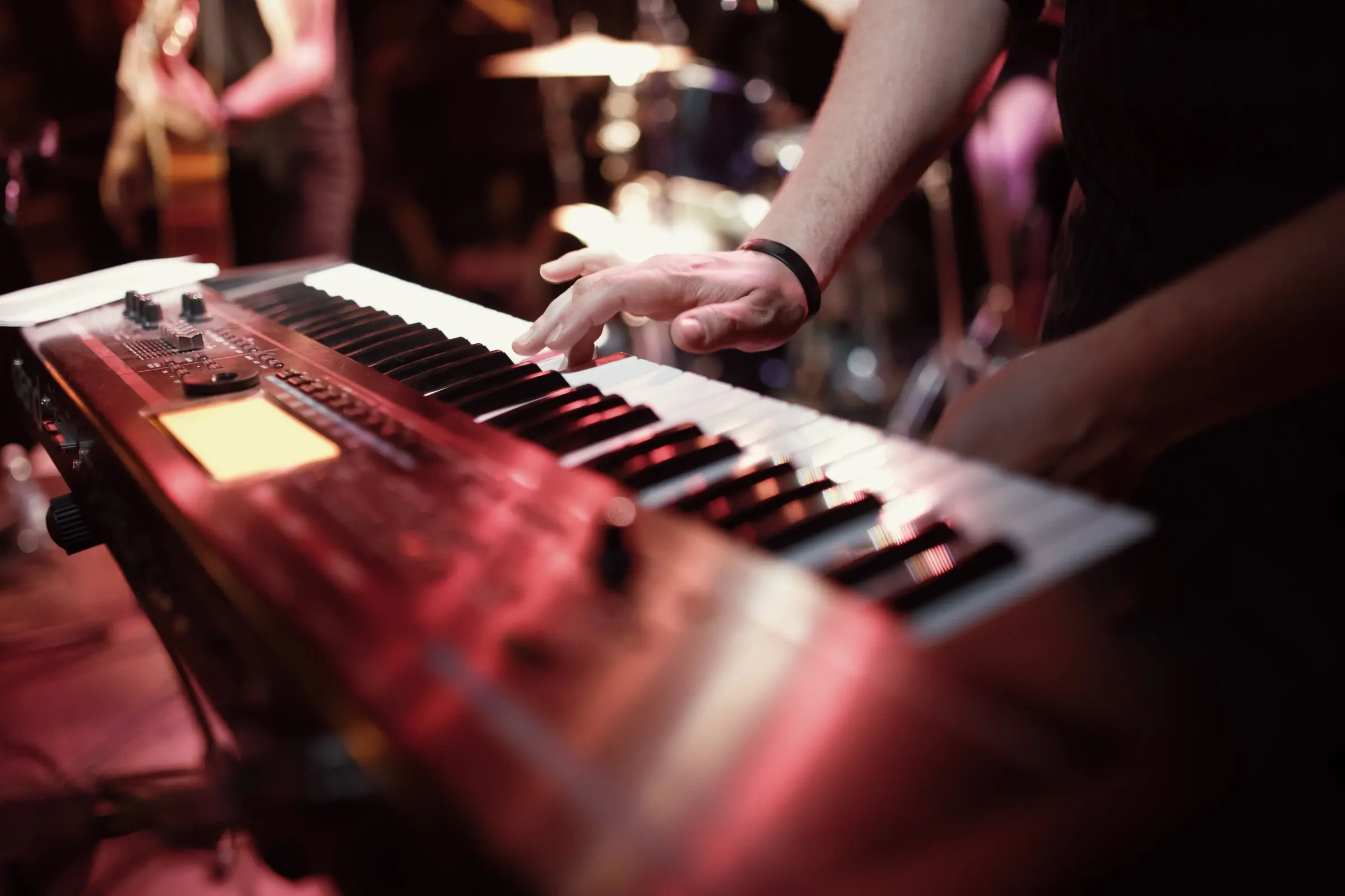 Hands playing a red keyboard synthesiser on stage.