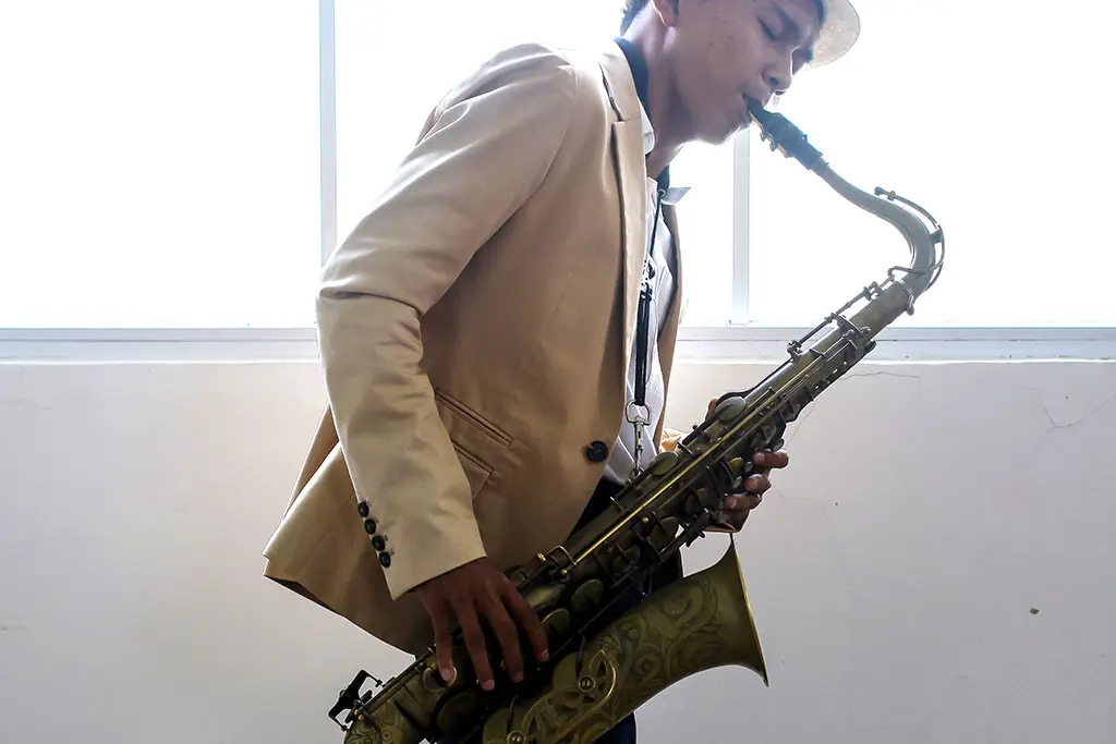 Man in a beige jacket playing a tenor saxophone