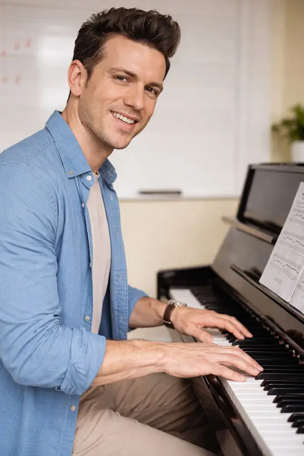 Man in a blue shirt playing an upright piano with sheet music