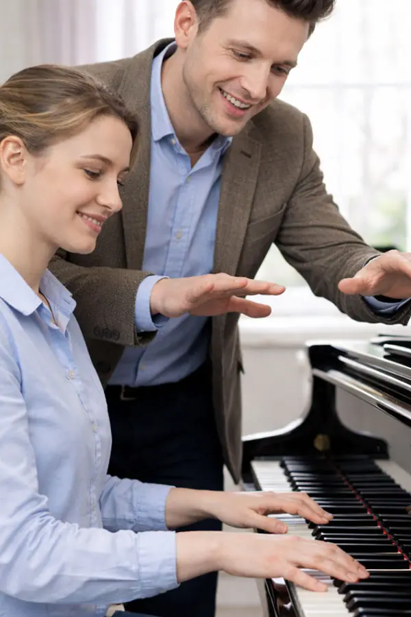 Man guiding a woman as she plays piano