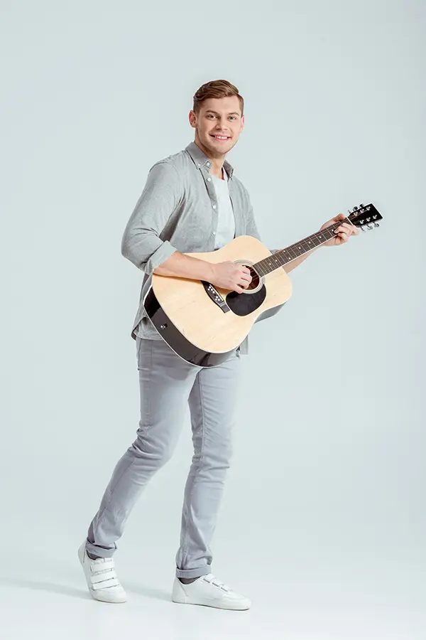 Man standing with an acoustic guitar against a plain background