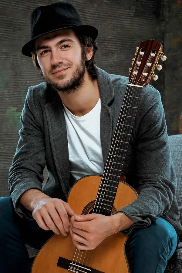 Man in a hat sitting with a classical guitar