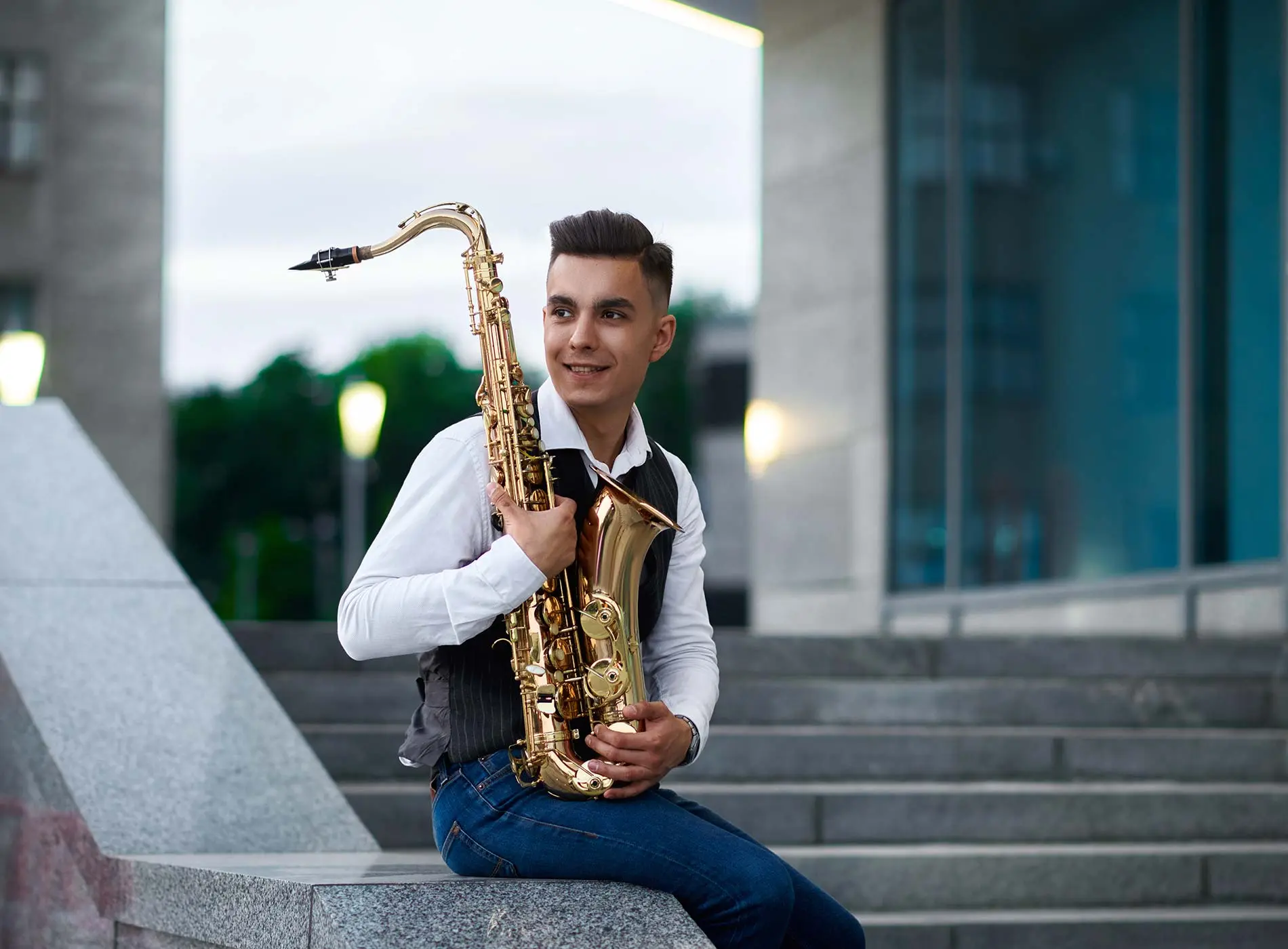 Man sitting near stairs by holding saxophone