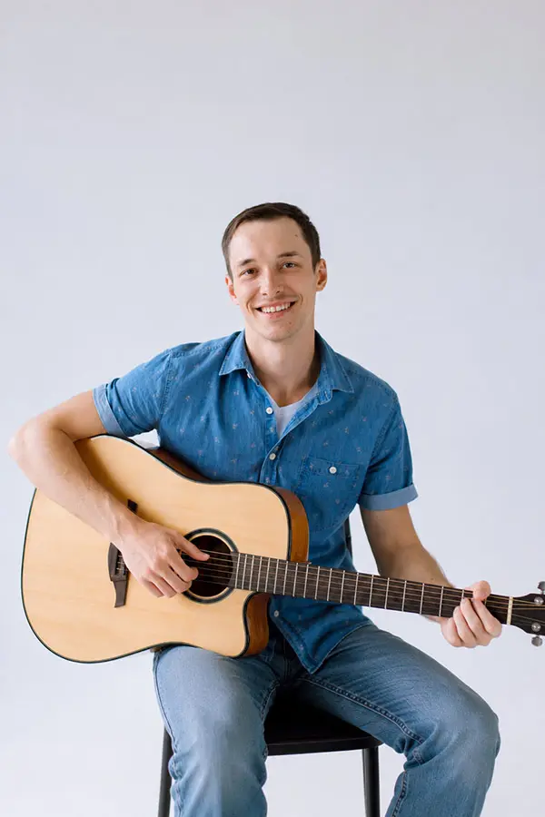 Smiling seated man in a blue shirt playing acoustic guitar