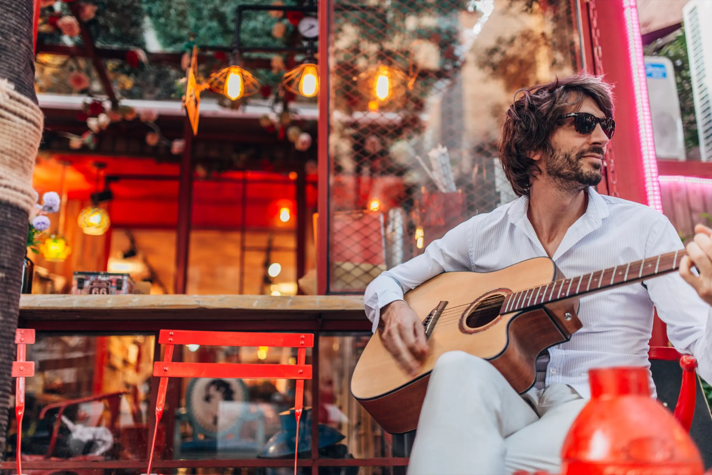 Man in sunglasses playing an acoustic guitar outside a café.