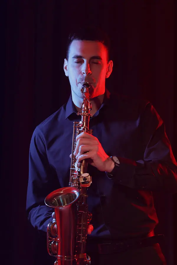Man playing alto saxophone under red stage lighting