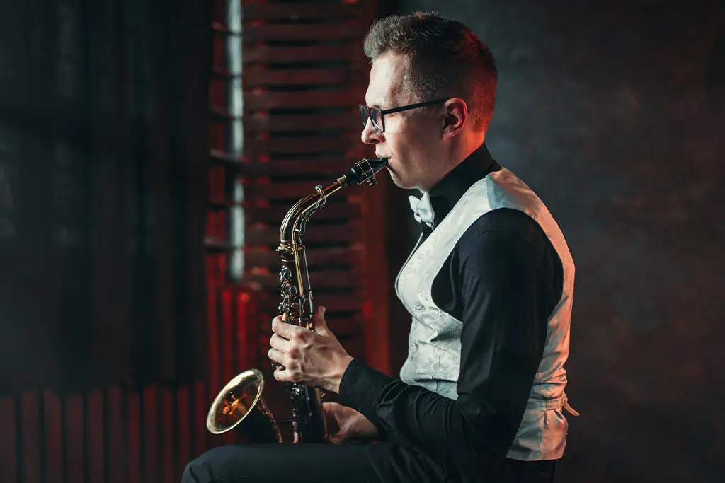 Man with glasses playing alto saxophone in a silver waistcoat