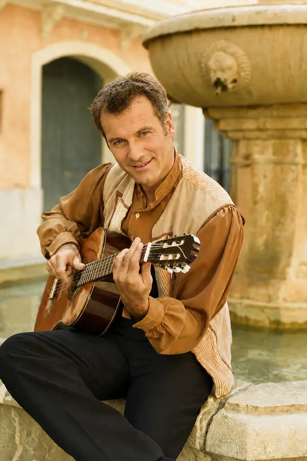 Man playing a classical guitar beside an outdoor fountain