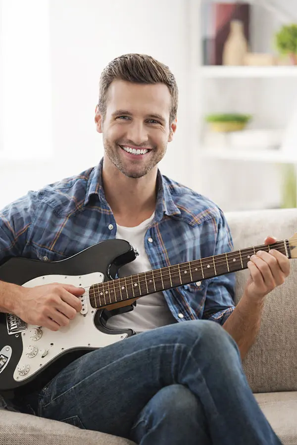 Smiling man playing an electric guitar on a sofa