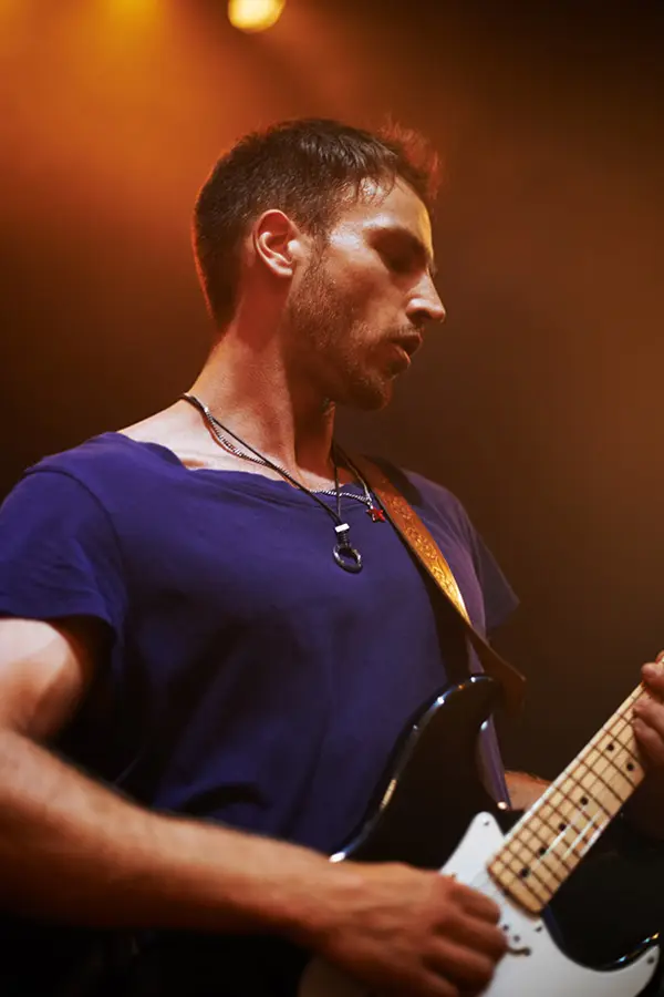 Man playing electric guitar on stage under warm lights