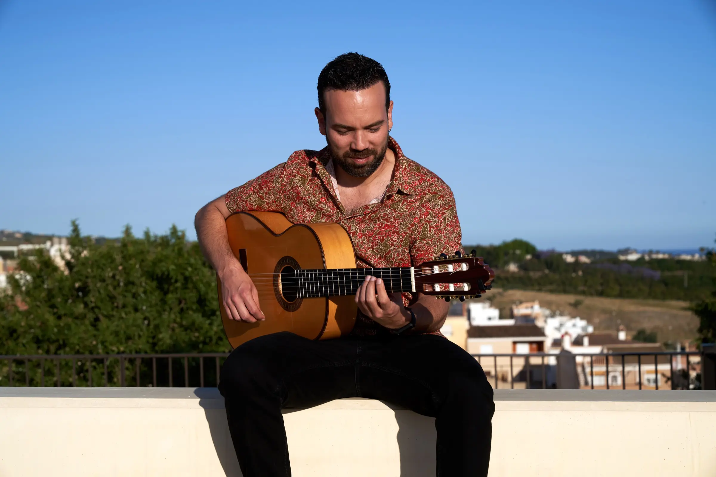 Man playing a flamenco guitar outdoors under a blue sky.