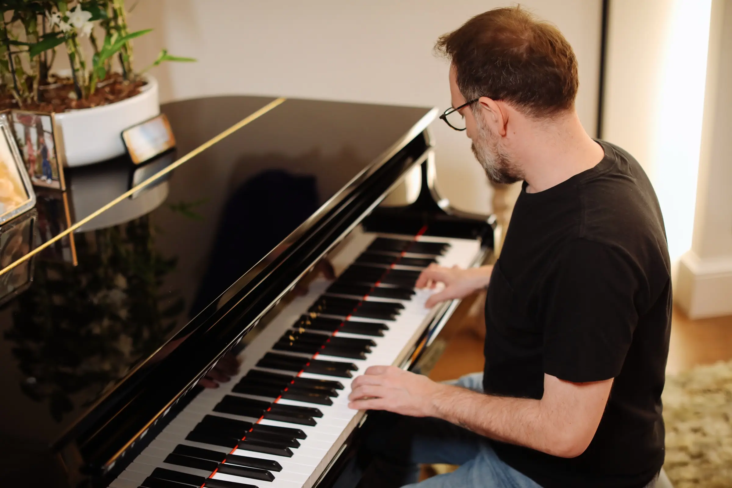 Man in glasses playing a grand piano at home.