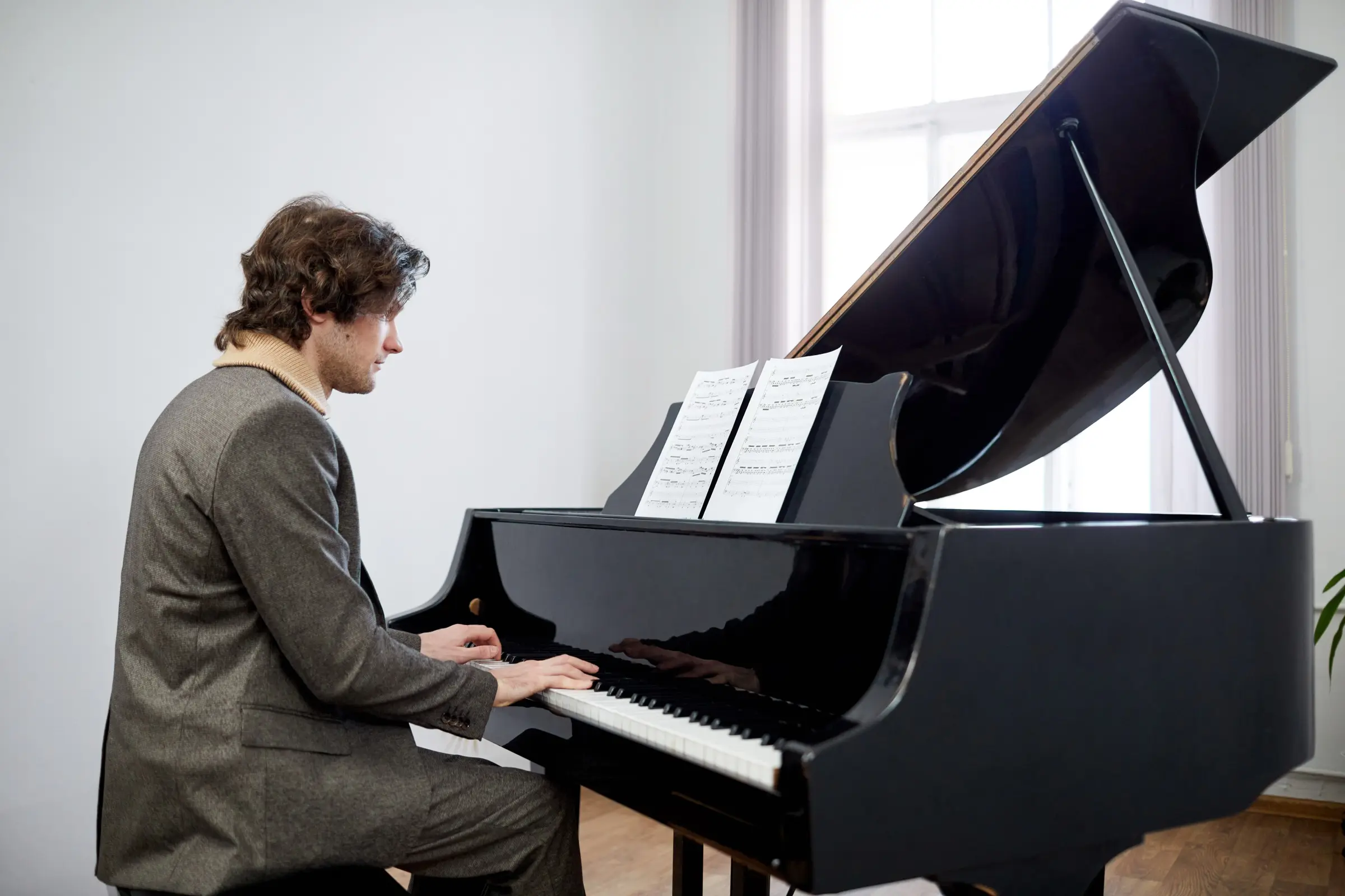 Man playing a black grand piano in a bright room.