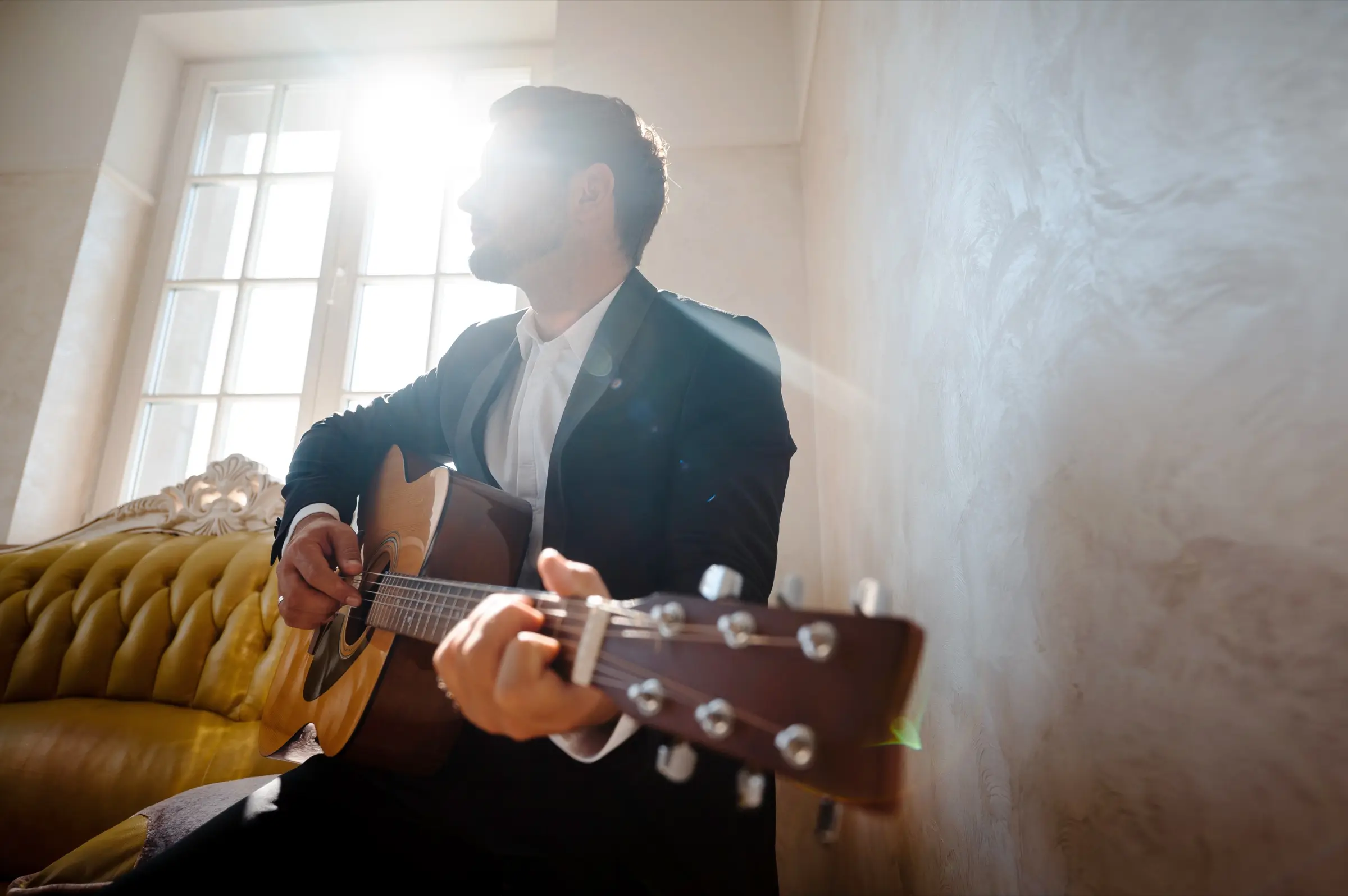 Man playing an acoustic guitar in a sunlit room.