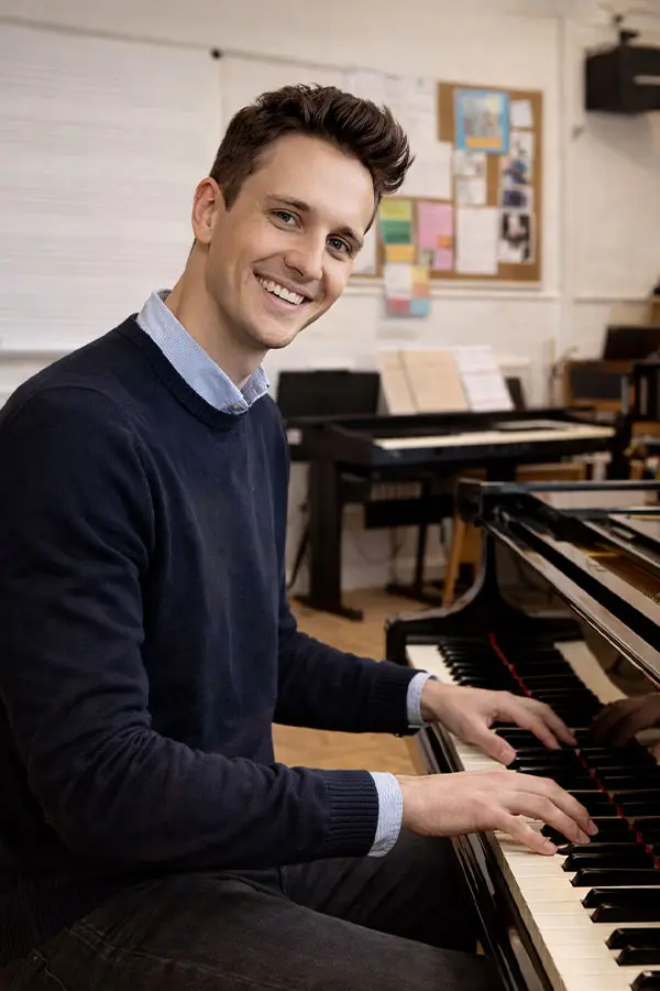 Smiling man playing piano in a music classroom