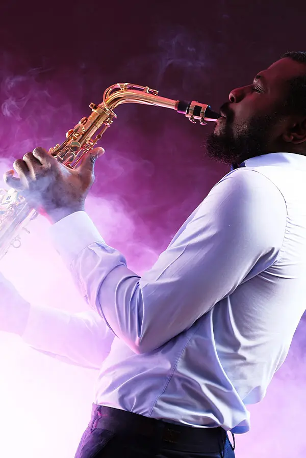 Man in a white shirt playing saxophone in purple stage smoke