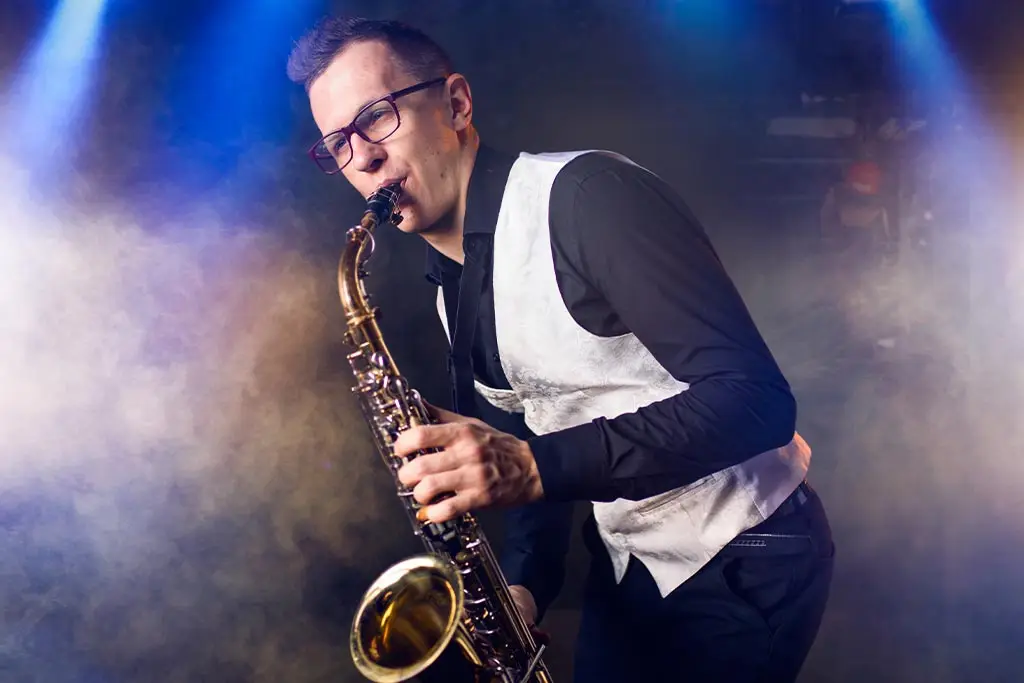 Man with glasses playing saxophone under stage lights