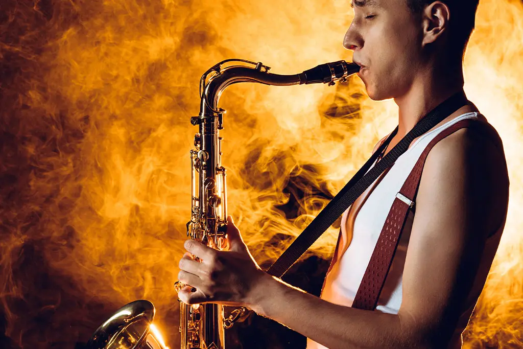 Man in a sleeveless top playing tenor saxophone in orange smoke