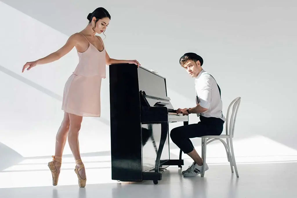 Man playing an upright piano beside a ballet dancer