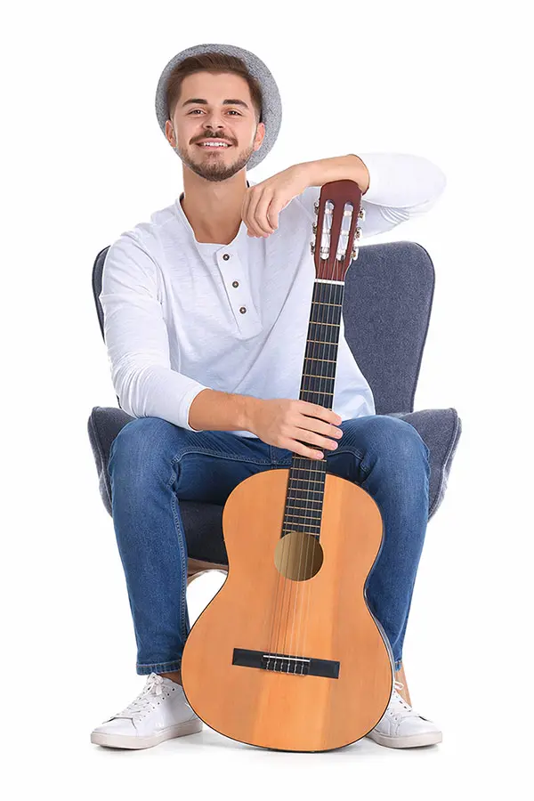 Man in a hat seated on a chair with a classical guitar