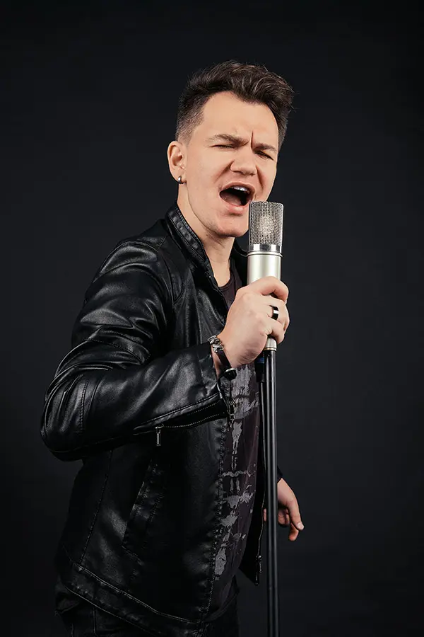 Man in a leather jacket singing into a studio microphone