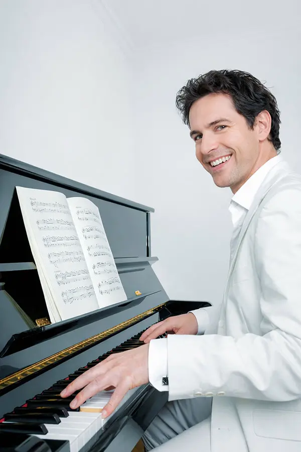 Smiling man in a white suit playing an upright piano