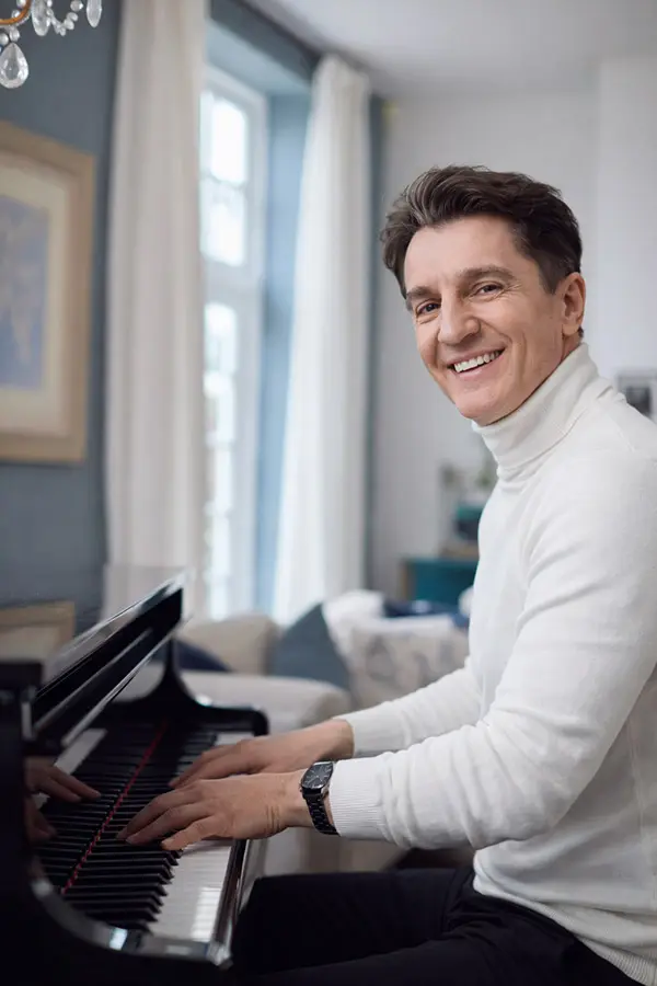 Man in a white turtleneck playing piano by a window