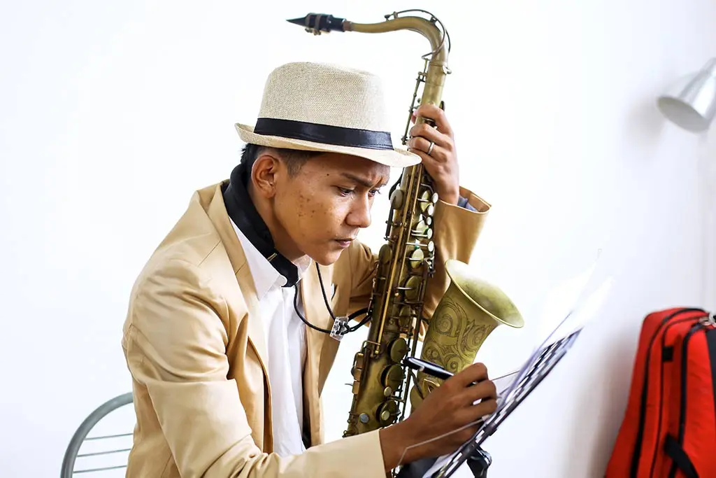 Man in a hat writing on sheet music while holding a saxophone