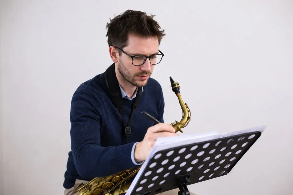 Man writing on paper while holding an alto saxophone
