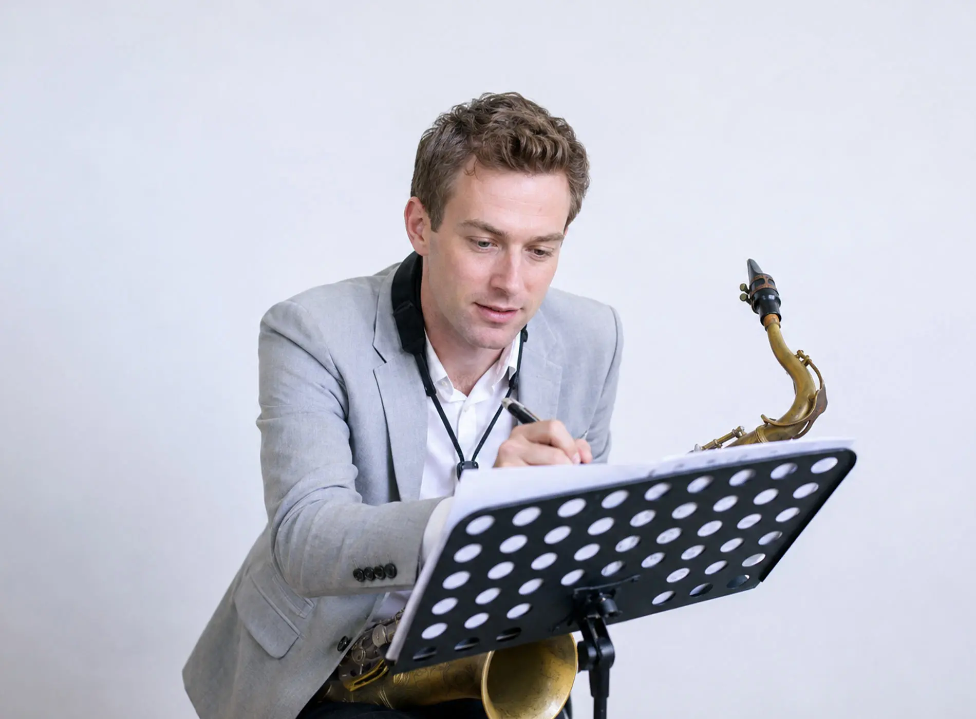 British man with saxophone and suit writing down on music paper