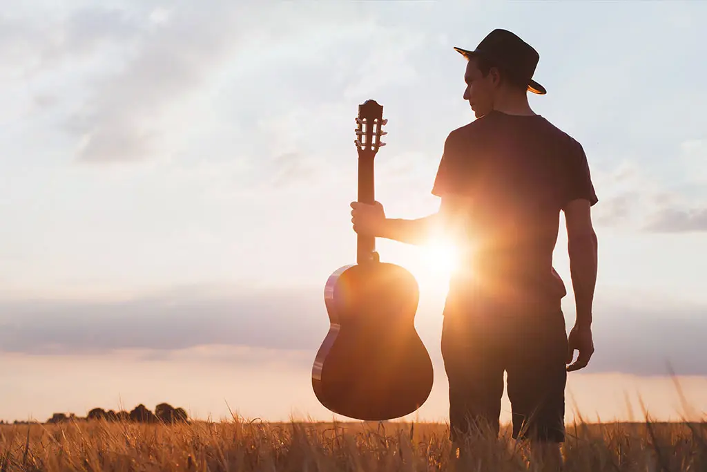 Image of musician with guitar at sunset field