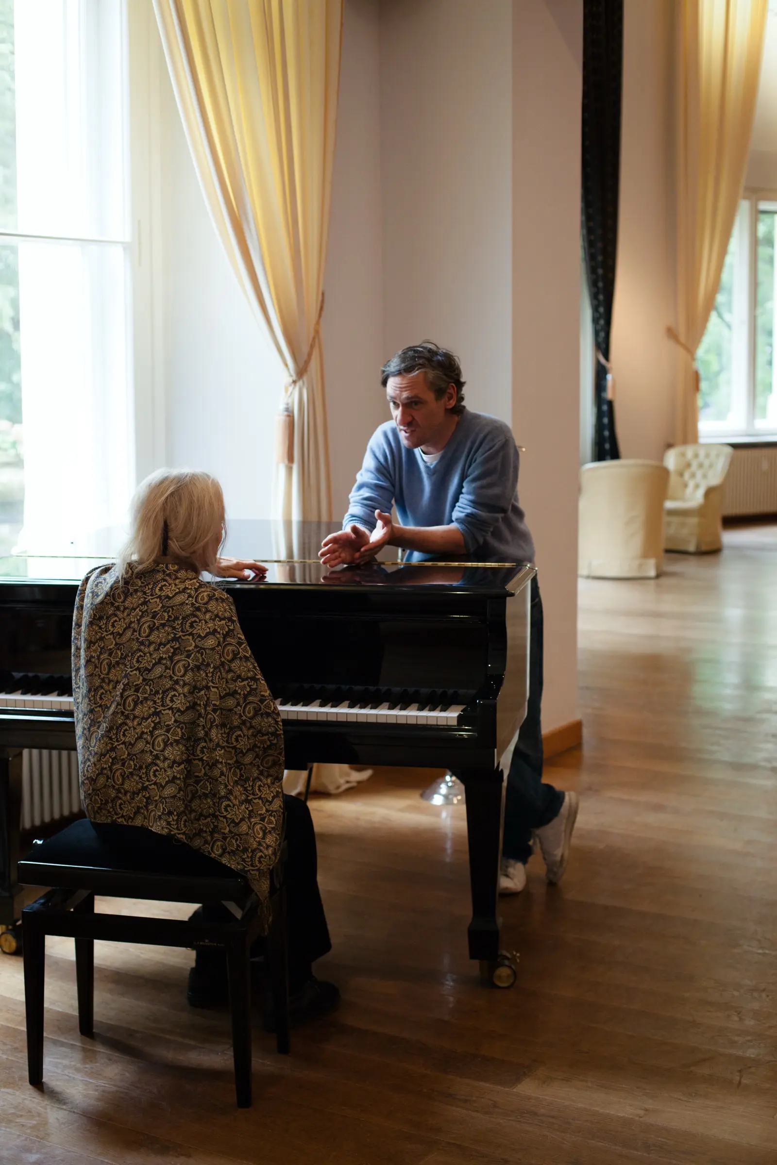 Older woman at a grand piano with her teacher sitting beside her.