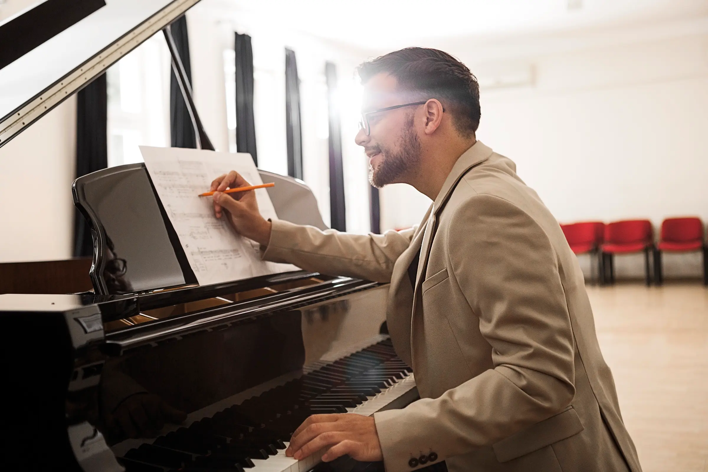 Pianist writing on sheet music while sitting at a grand piano.