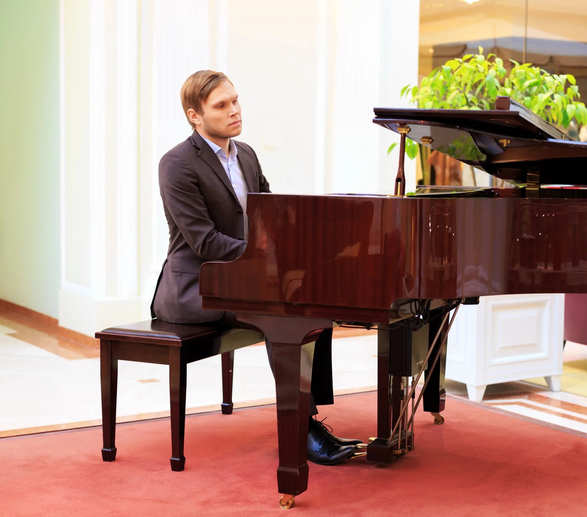 Pianist in a suit playing a grand piano in a bright room.