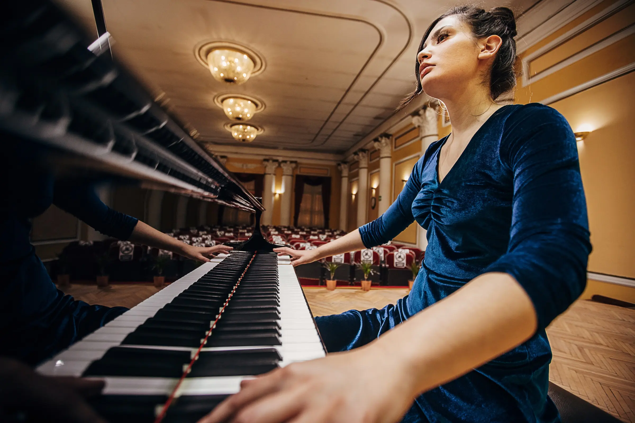 Pianist in a velvet dress playing a grand piano in an empty concert hall.