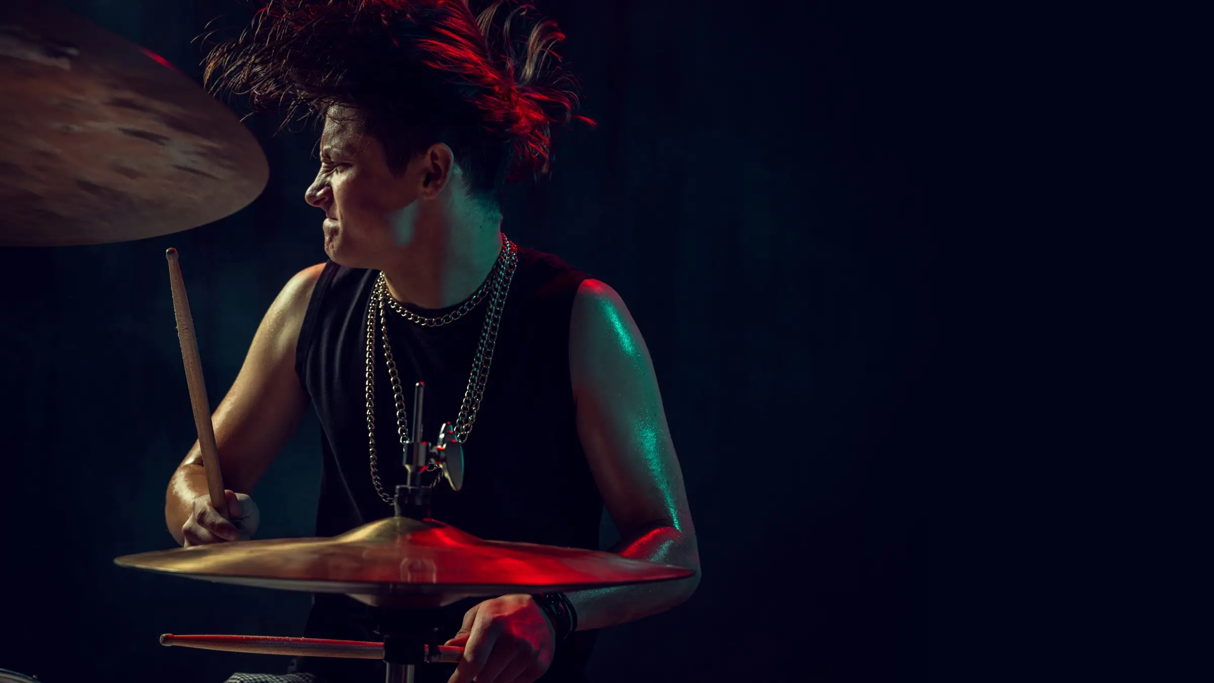 A rock drummer mid-performance under red and blue stage lights