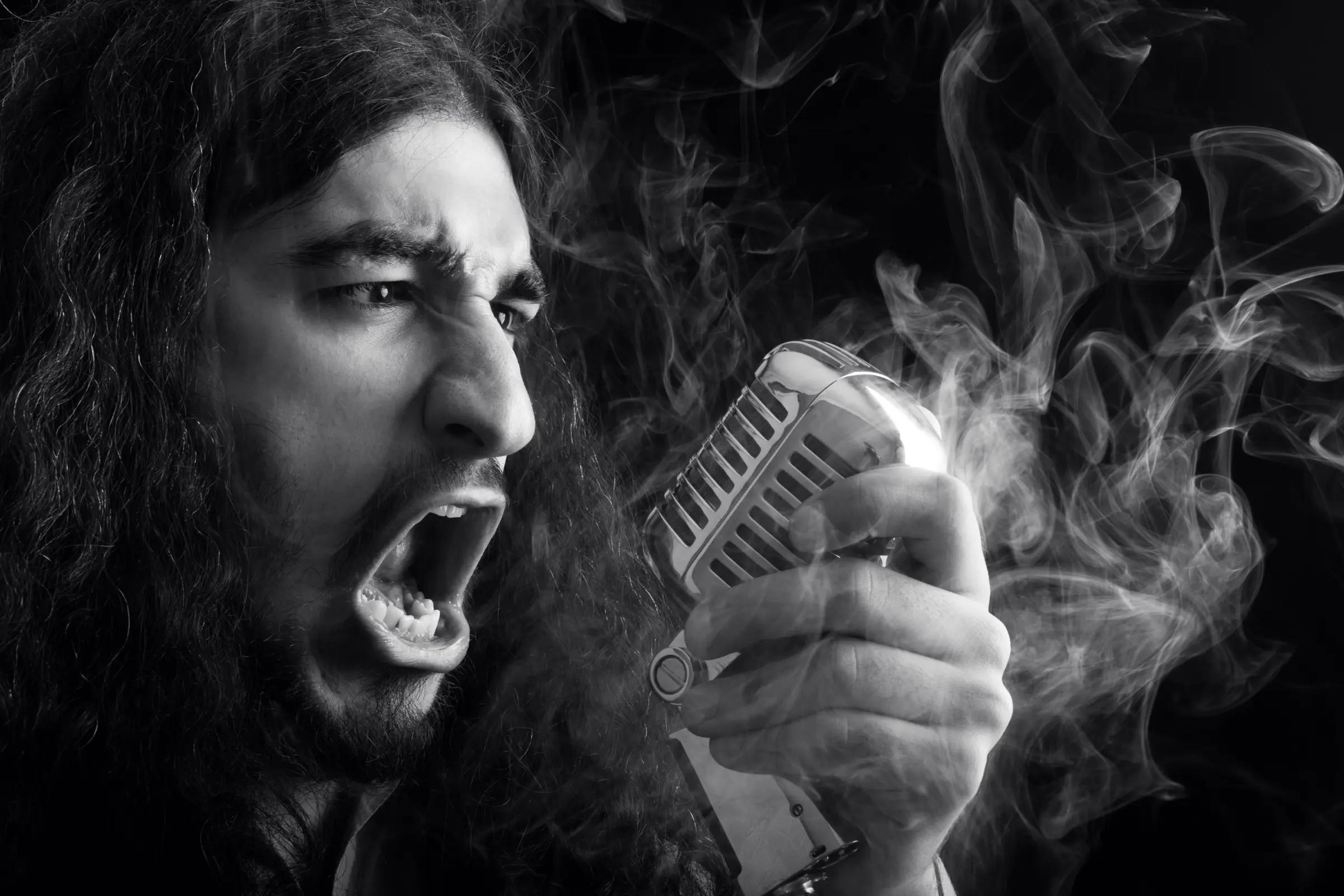 Long-haired singer shouting into a vintage microphone, in black and white.