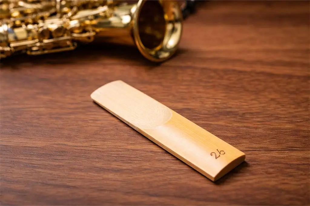 Saxophone reed on a wooden table beside a saxophone