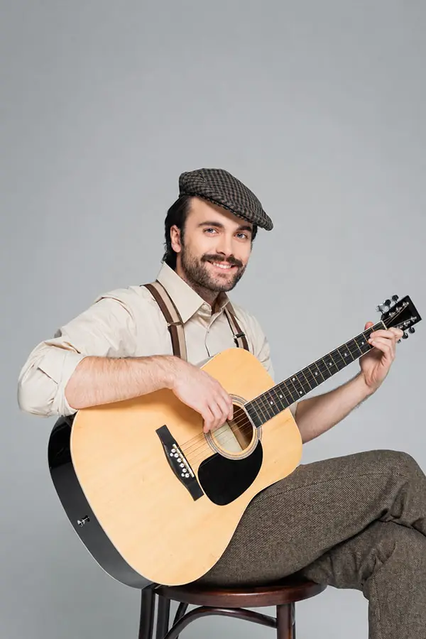 Smiling man seated on a stool holding an acoustic guitar