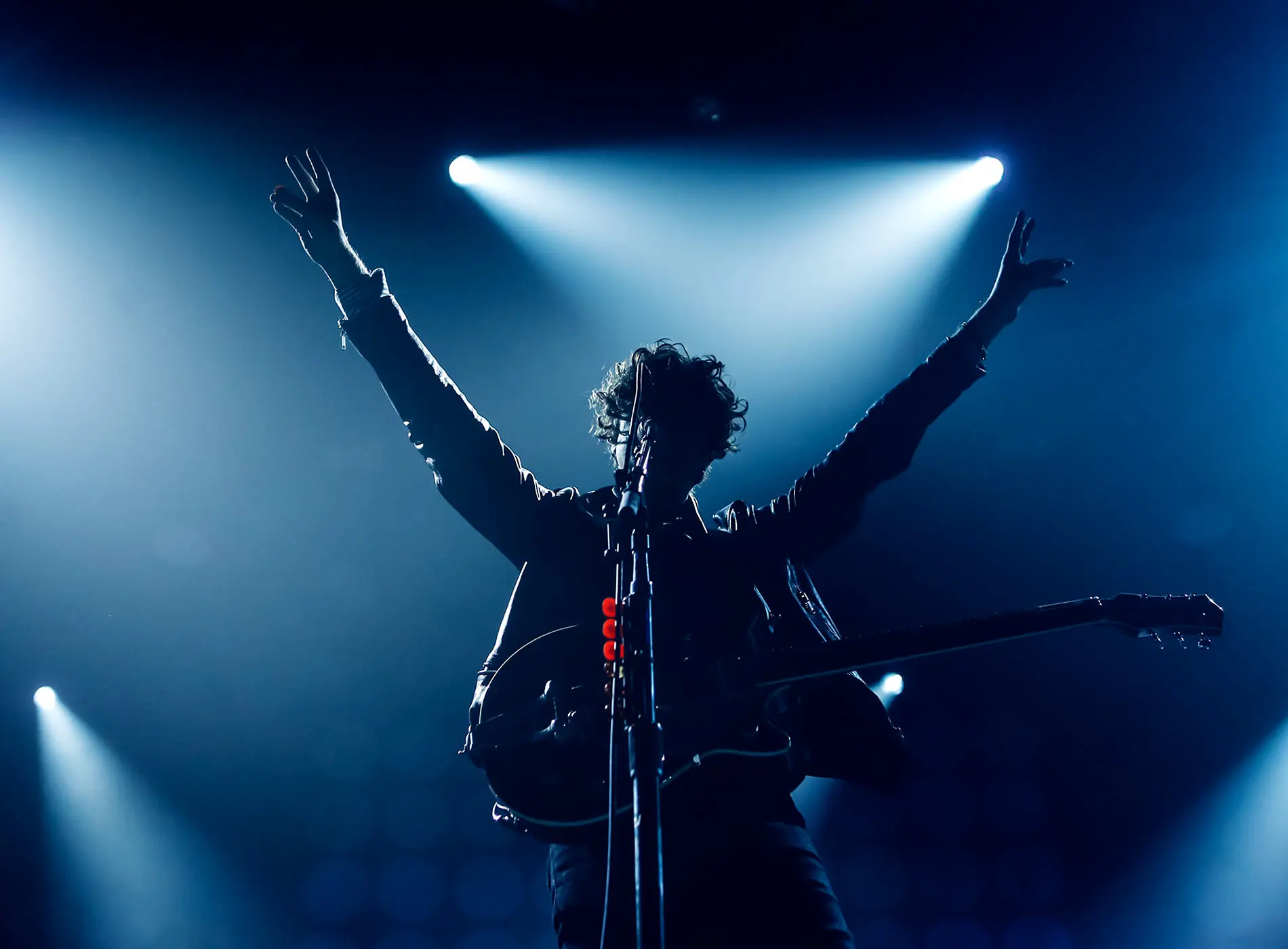 A vocalist silhouette with the guitar singing with the hands raised up in blue lights