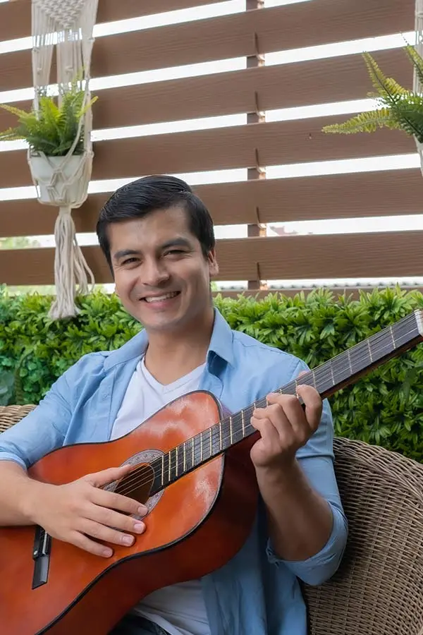 Smiling man in a blue shirt seated outdoors with a classical guitar