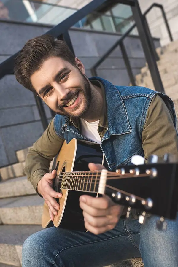 Smiling man sitting on stairs with an acoustic guitar