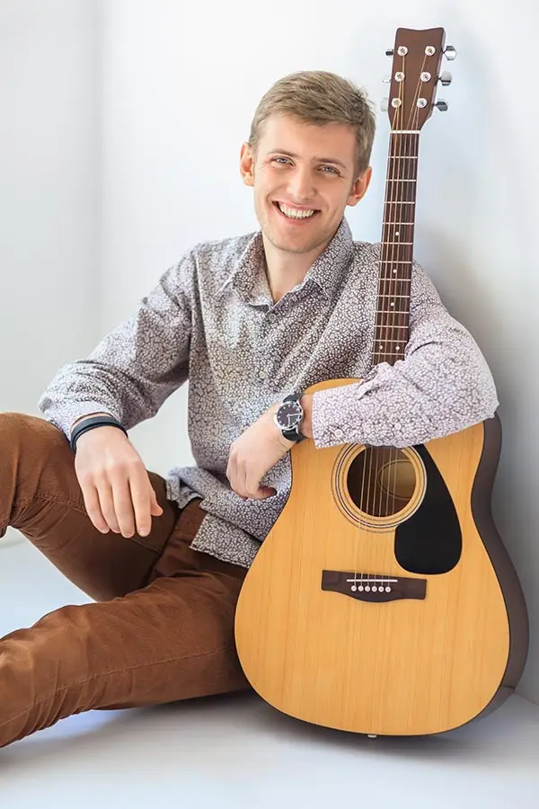 Smiling man sitting beside an acoustic guitar